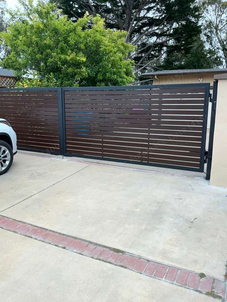 Brown horizontal-slat automatic driveway gate in a black steel frame