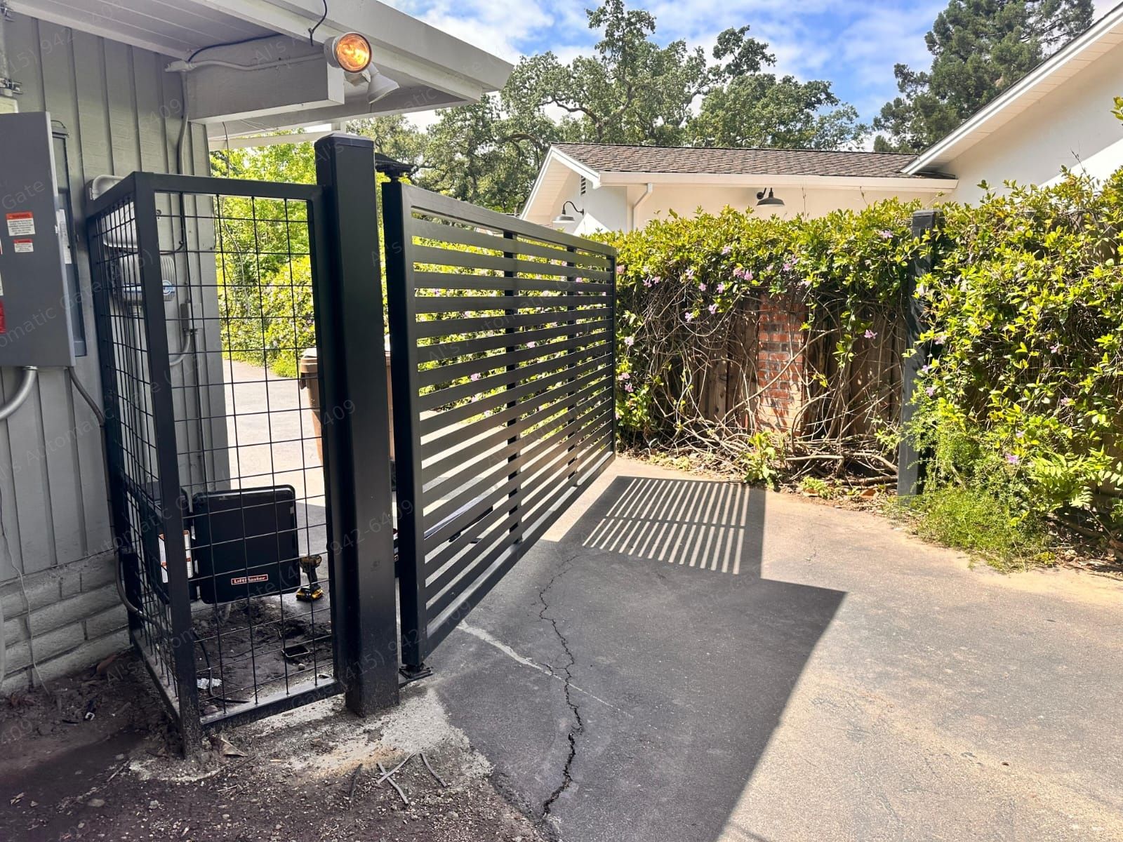 Black slat swing driveway gate with LiftMaster operator in a mesh enclosure